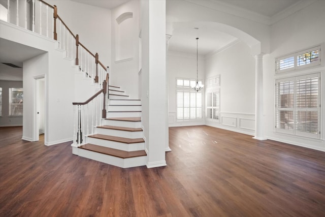 stairs with crown molding, hardwood / wood-style flooring, an inviting chandelier, a towering ceiling, and decorative columns