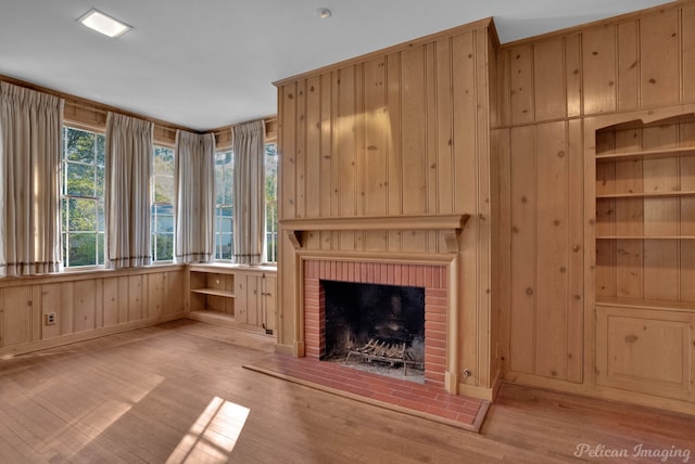 unfurnished living room with wood walls, light hardwood / wood-style flooring, built in features, and a brick fireplace