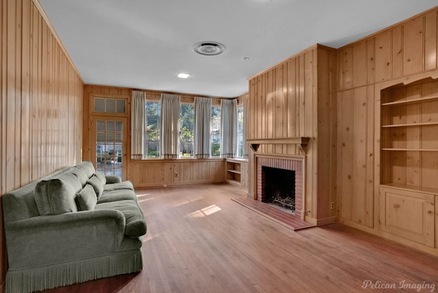 living room with light hardwood / wood-style flooring, a brick fireplace, wooden walls, and built in features