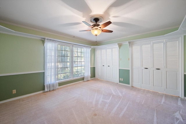 unfurnished bedroom featuring ceiling fan, ornamental molding, light colored carpet, and multiple closets