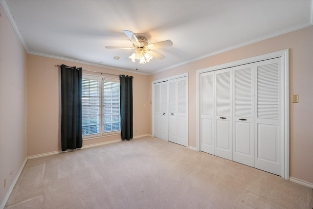 unfurnished bedroom featuring multiple closets, light colored carpet, crown molding, and ceiling fan