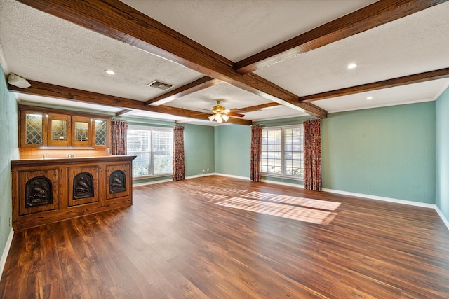 unfurnished living room featuring visible vents, wood finished floors, beamed ceiling, baseboards, and a textured ceiling