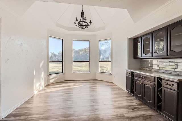 unfurnished dining area with light hardwood / wood-style floors, an inviting chandelier, and a tray ceiling