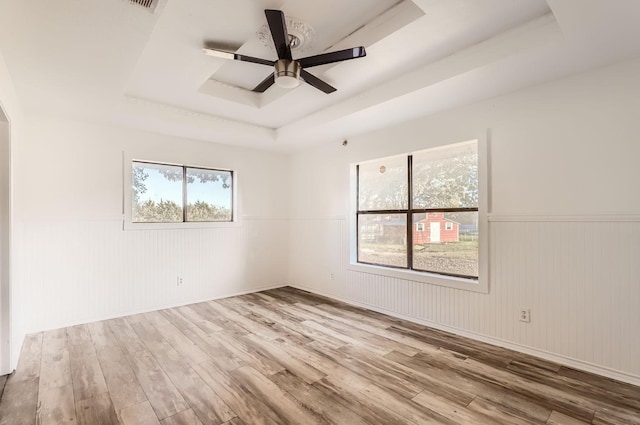 spare room with a raised ceiling, ceiling fan, light hardwood / wood-style floors, and wood walls