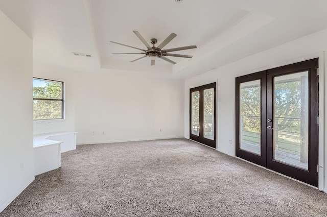 empty room with a raised ceiling, carpet floors, a wealth of natural light, and french doors