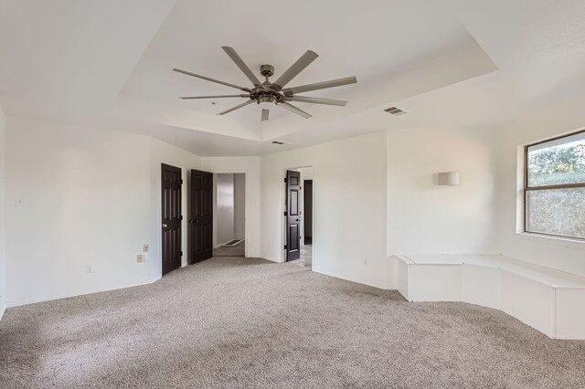 empty room with ceiling fan, light carpet, and a tray ceiling