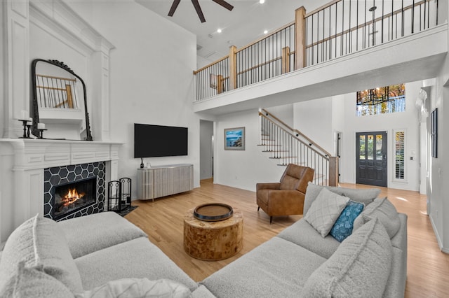 living room with a high ceiling, a tile fireplace, ceiling fan, and light wood-type flooring