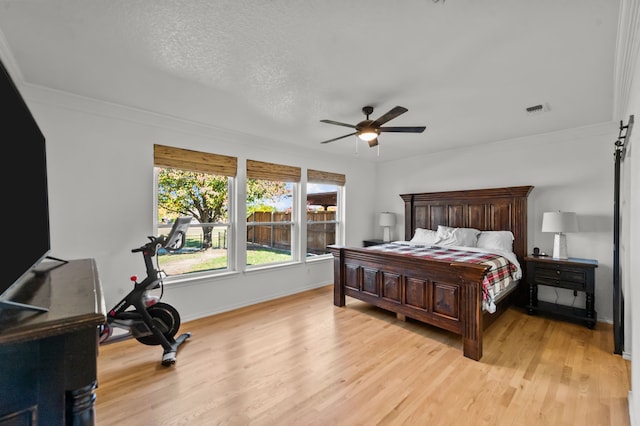 bedroom featuring light hardwood / wood-style flooring, a textured ceiling, ornamental molding, ceiling fan, and a barn door