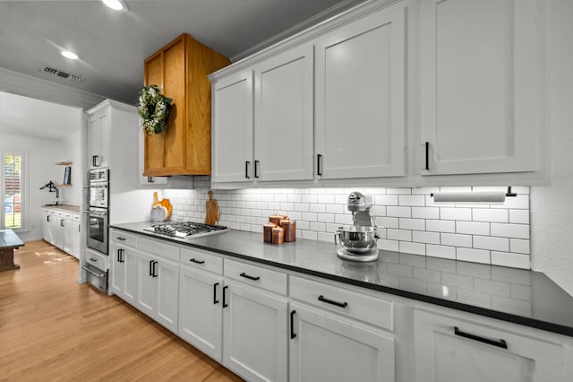 kitchen featuring crown molding, light hardwood / wood-style flooring, appliances with stainless steel finishes, white cabinetry, and decorative backsplash