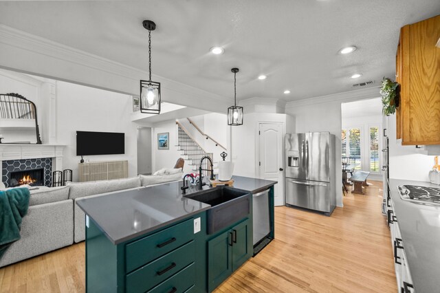 kitchen featuring a tile fireplace, appliances with stainless steel finishes, light hardwood / wood-style floors, crown molding, and a center island with sink