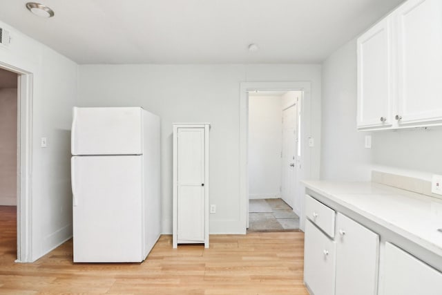 kitchen with light wood finished floors, baseboards, freestanding refrigerator, light countertops, and white cabinetry