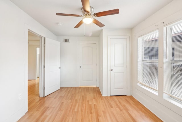 unfurnished bedroom with a ceiling fan, multiple windows, visible vents, and light wood-style floors