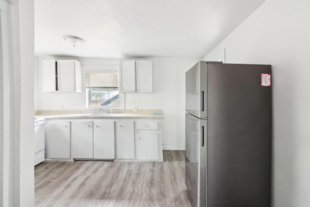 kitchen with light countertops, a sink, freestanding refrigerator, and white cabinets