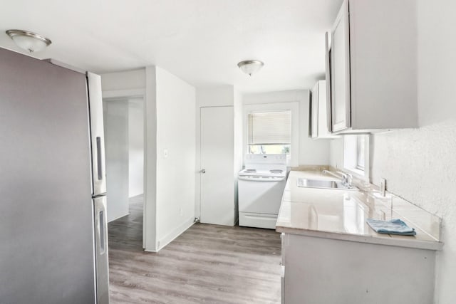 kitchen featuring light wood finished floors, electric stove, freestanding refrigerator, light countertops, and a sink