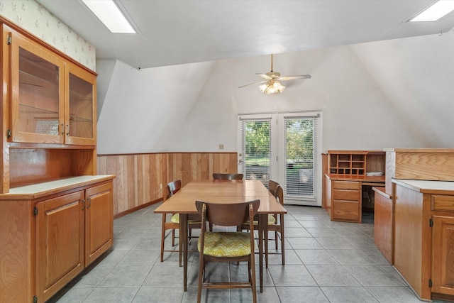 tiled dining space with wood walls, ceiling fan, and vaulted ceiling