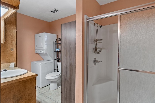 bathroom featuring walk in shower, vanity, stacked washer / dryer, tile patterned flooring, and toilet