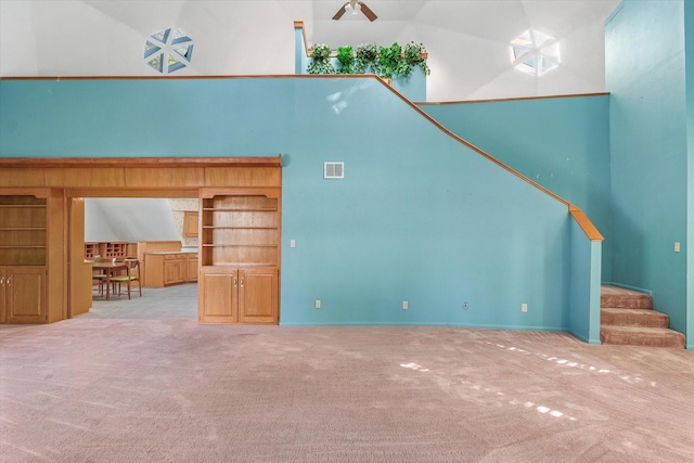 unfurnished living room featuring built in features, high vaulted ceiling, and light colored carpet