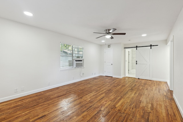 spare room with cooling unit, ceiling fan, wood-type flooring, and a barn door