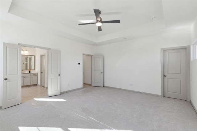 unfurnished bedroom featuring light carpet, baseboards, a raised ceiling, and ensuite bathroom