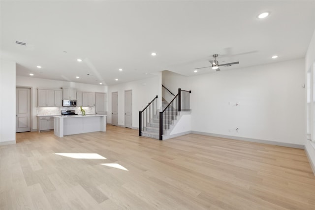 unfurnished living room featuring light wood-style floors, recessed lighting, stairway, and baseboards