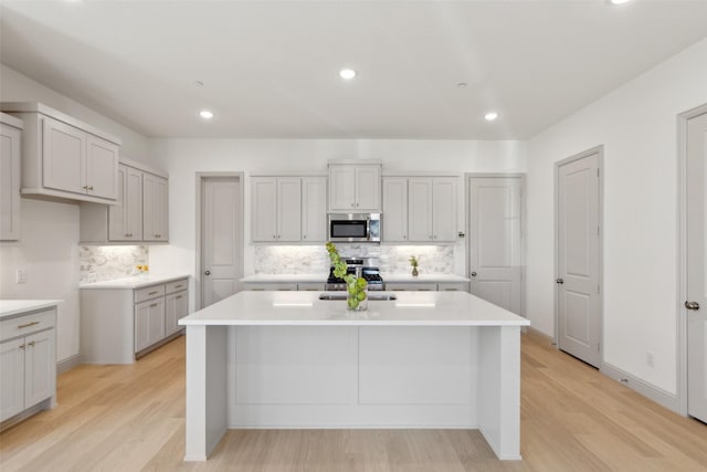 kitchen featuring stainless steel appliances, light wood-style flooring, light countertops, and a center island with sink