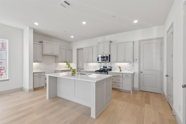 kitchen with a sink, visible vents, light countertops, appliances with stainless steel finishes, and a center island with sink