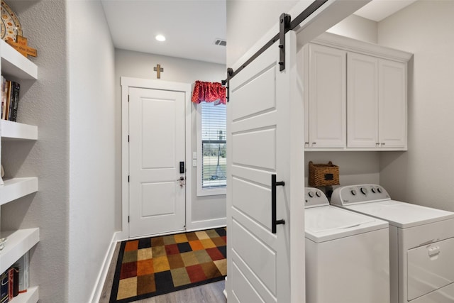 laundry room with washer and dryer, a barn door, cabinets, and light wood-type flooring