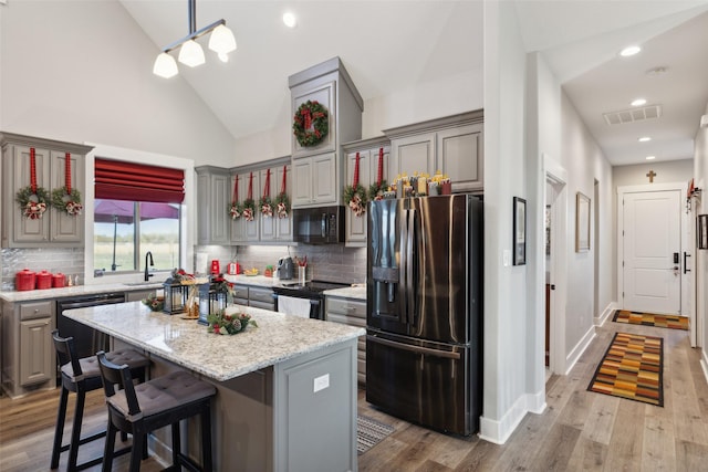 kitchen featuring light stone countertops, light wood-type flooring, stainless steel appliances, decorative light fixtures, and a center island