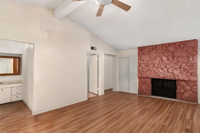 unfurnished living room with ceiling fan, beam ceiling, light hardwood / wood-style floors, and a stone fireplace