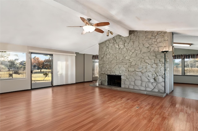 unfurnished living room featuring a stone fireplace, vaulted ceiling with beams, wood-type flooring, a textured ceiling, and ceiling fan