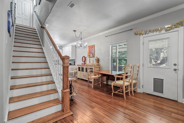 foyer entrance featuring crown molding, a notable chandelier, visible vents, stairway, and wood finished floors