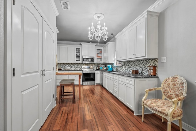 kitchen featuring dark countertops, visible vents, appliances with stainless steel finishes, glass insert cabinets, and white cabinetry