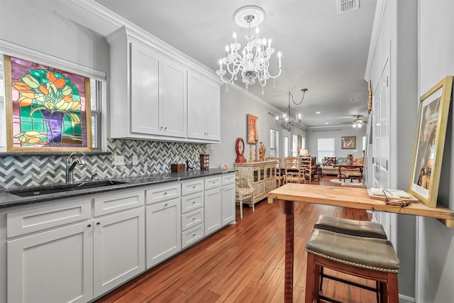 kitchen with sink, light hardwood / wood-style floors, decorative light fixtures, white cabinets, and ceiling fan with notable chandelier