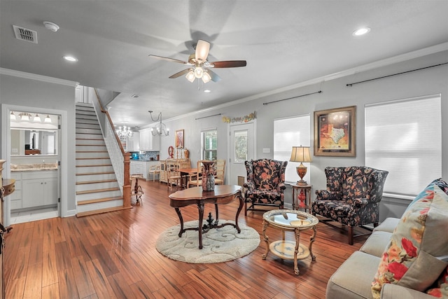 living room featuring wood-type flooring, ceiling fan with notable chandelier, and crown molding