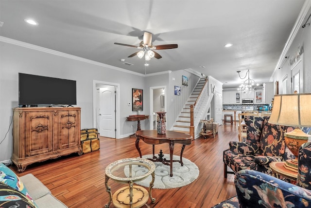 living area with stairs, ornamental molding, ceiling fan with notable chandelier, and wood finished floors