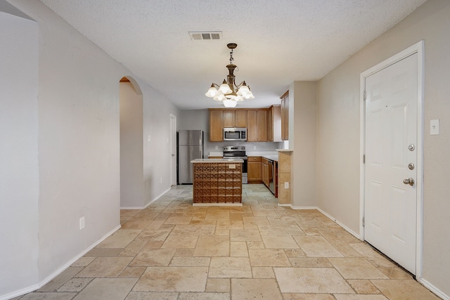 kitchen with hanging light fixtures, stainless steel appliances, a center island, and a textured ceiling