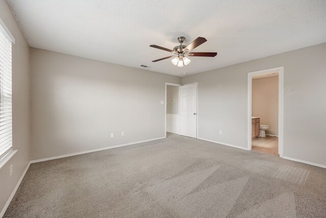 unfurnished bedroom with multiple windows, carpet flooring, connected bathroom, and ceiling fan