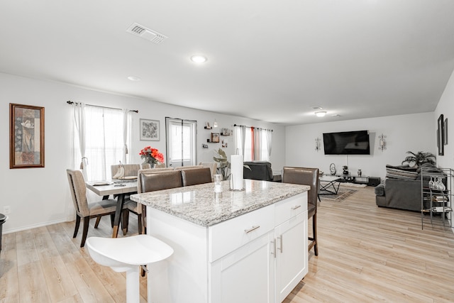 kitchen with a kitchen bar, light stone countertops, light hardwood / wood-style flooring, a center island, and white cabinetry