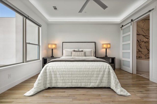 bedroom featuring light wood-type flooring, a barn door, and ceiling fan