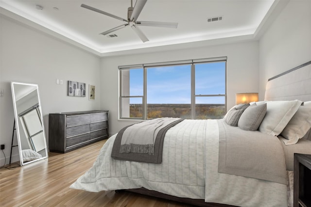 bedroom with a tray ceiling, ceiling fan, and light hardwood / wood-style floors