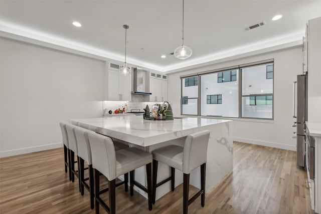 kitchen with light stone countertops, wall chimney exhaust hood, decorative light fixtures, hardwood / wood-style flooring, and white cabinets