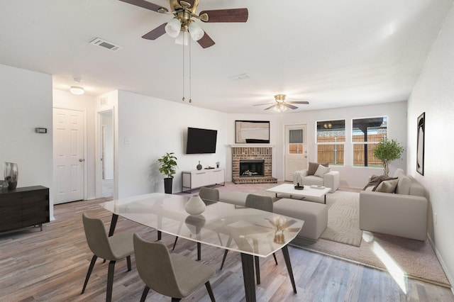 living room featuring ceiling fan, light wood-type flooring, and a fireplace