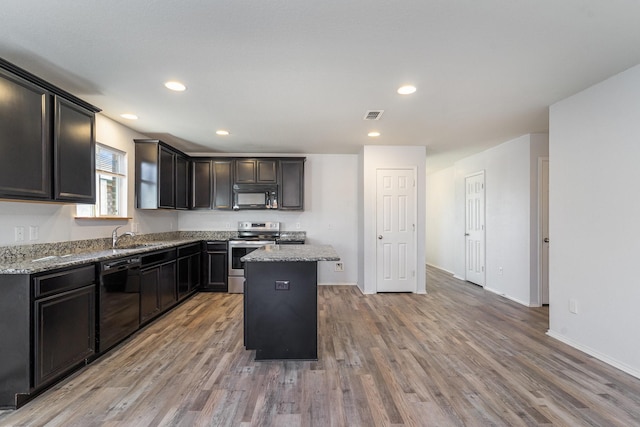 kitchen with black appliances, a center island, light stone countertops, and hardwood / wood-style floors