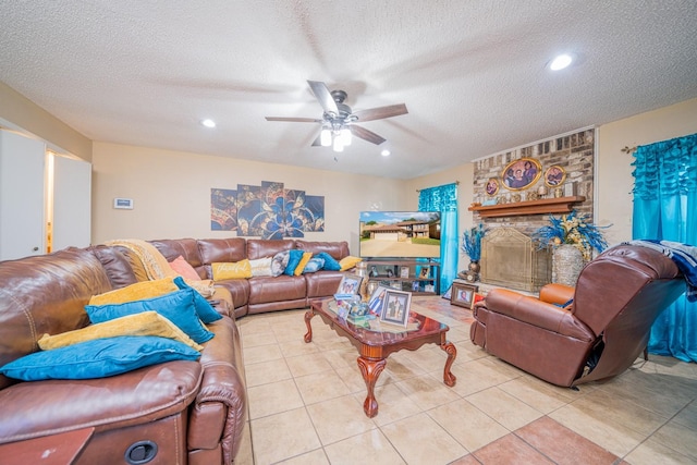 living room featuring ceiling fan, a fireplace, light tile patterned floors, and a textured ceiling