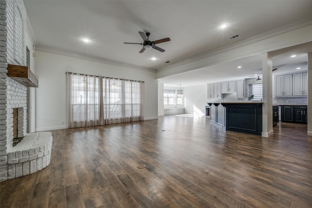 unfurnished living room featuring ceiling fan, a large fireplace, dark hardwood / wood-style flooring, and ornamental molding