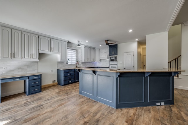 kitchen with stainless steel microwave, blue cabinets, sink, a kitchen island, and light hardwood / wood-style floors