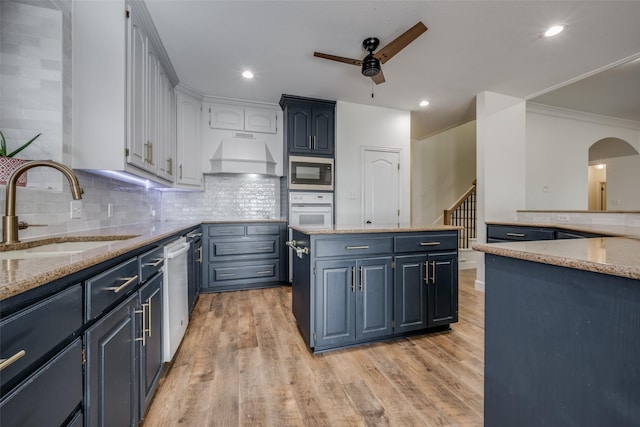 kitchen with light stone countertops, light wood-type flooring, custom range hood, stainless steel appliances, and sink