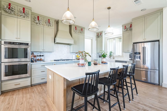 kitchen with premium range hood, appliances with stainless steel finishes, hanging light fixtures, a kitchen breakfast bar, and a center island