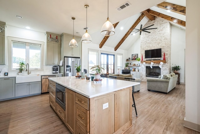 kitchen featuring sink, a large fireplace, hanging light fixtures, a center island, and stainless steel appliances