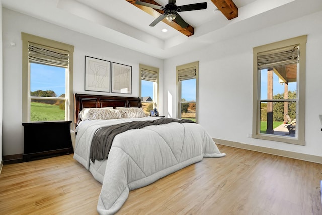 bedroom featuring beam ceiling, ceiling fan, light hardwood / wood-style floors, and a tray ceiling